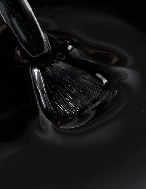 A brush is submerged in or moving through thick black liquid, creating ripples and reflections.