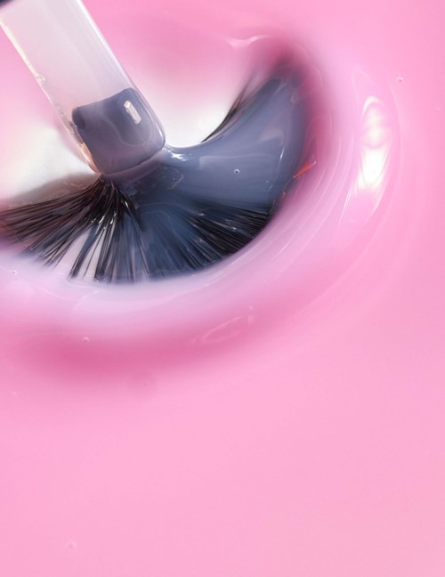 A makeup brush is applying black eyeshadow on a pink surface.