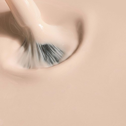 A close-up of a makeup brush blending beige foundation or cream on skin.