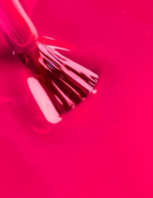 A metallic brush with black bristles on a bright pink background.