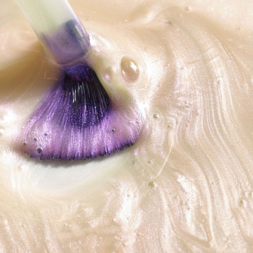 A makeup brush is applying purple eyeshadow on skin, creating a colorful and artistic effect.