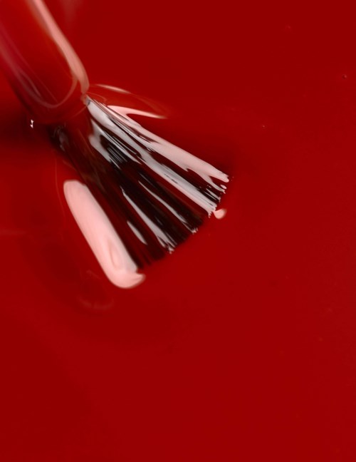 A nail polish brush painting pink polish onto a red surface.