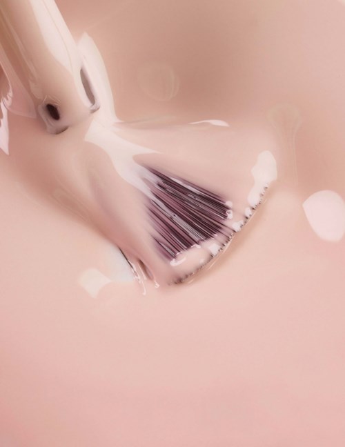 A makeup brush with white foam on it, lying on a pink surface.