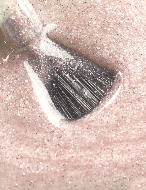A makeup brush spreads pink glitter on skin. The scene shows close-up of sparkle and soft texture.