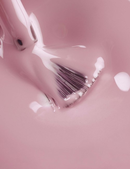 A makeup brush is covered in pink paint or liquid, blending smoothly on a pink surface.
