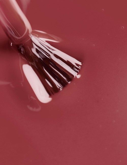 A paintbrush touching pink paint surface.