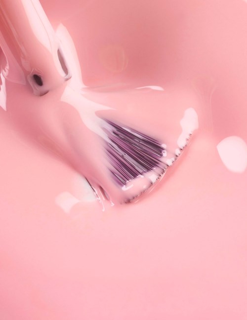A makeup brush is dipped in pink liquid, creating bubbles and foam around it.