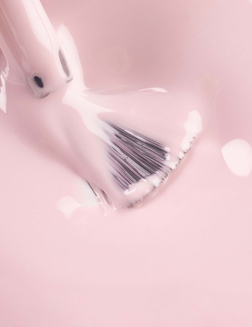 A hand with a brush is mixing pink paint in a container.