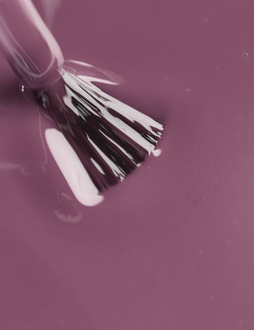 A paintbrush is dipped in pinkish paint, creating brush strokes on a pink surface.