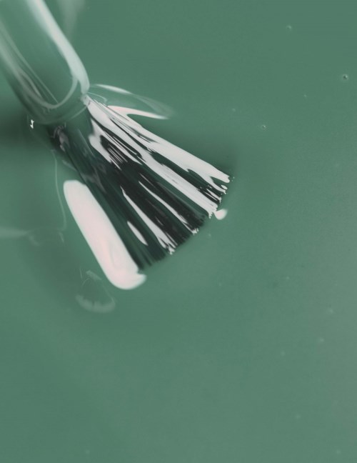 A brush is cleaning or applying something on a smooth green surface.
