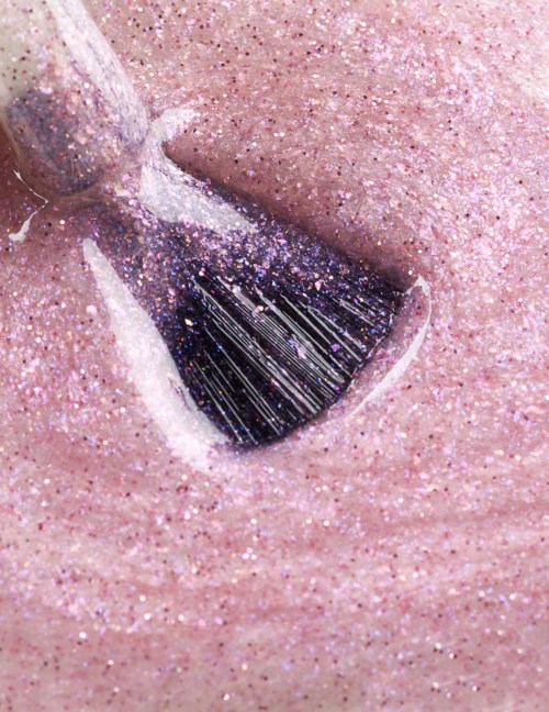 En nagel med glittrig rosa nagellack och ett mörkt, glittrigt triangelmönster.