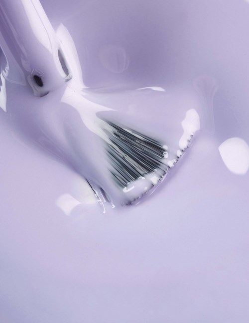 A makeup brush is submerged in a white liquid with some foam, creating a soft, blurred background.