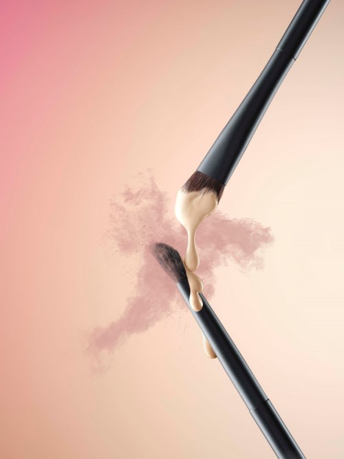Two makeup brushes with powder and cream blending in the middle on a pink background.
