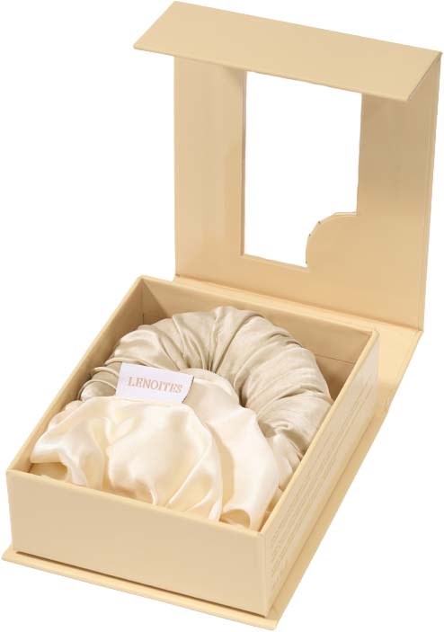 A cream-colored box contains a silk pillow and a satin bag. The box has a clear window on the lid.