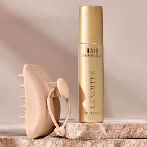 En beige hårbørste med stropp og en gullfarget L'Occitane hårspray på en steinoverflate.