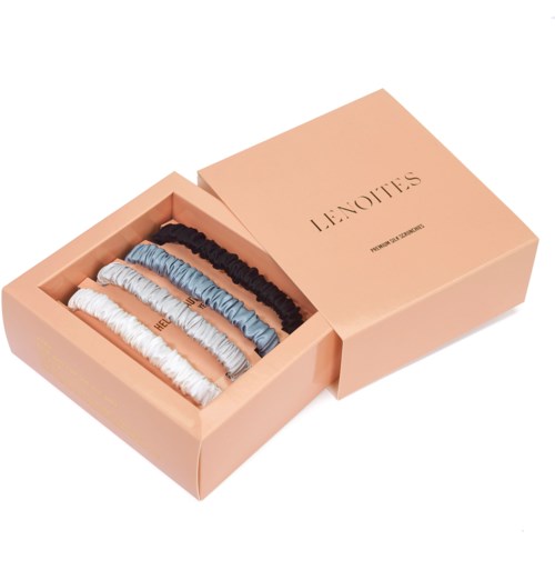 A pink box with six colored hair elastics: white, light blue, black, dark blue, and beige.