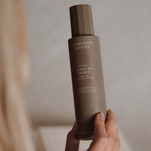 Eine Hand hält eine beige Sprühflasche mit der Aufschrift 'LERNBERGER STAFSING' und 'Leave-In Primer'.