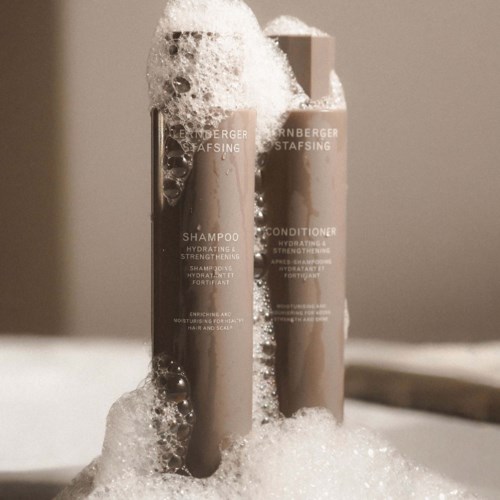 Zwei Shampoo- und Conditioner-Flaschen sind mit Schaum bedeckt und stehen aufrecht. Die Flaschen sind mit Produktdetails gekennzeichnet.