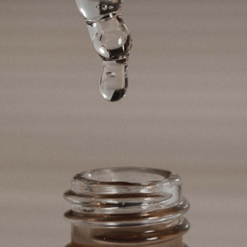 Ein Wassertropfen fällt in eine kleine Glasflasche und erzeugt Wellen darin.