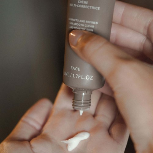 Eine Hand gibt Creme aus einer Tube auf die Handfläche. Die Tube ist grau und hat Anweisungen und Text.