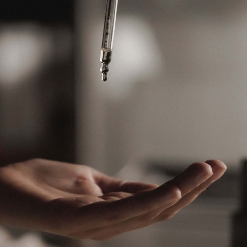 Eine Hand unter einer Pipette, die Flüssigkeit in einem klinischen Umfeld abgibt.
