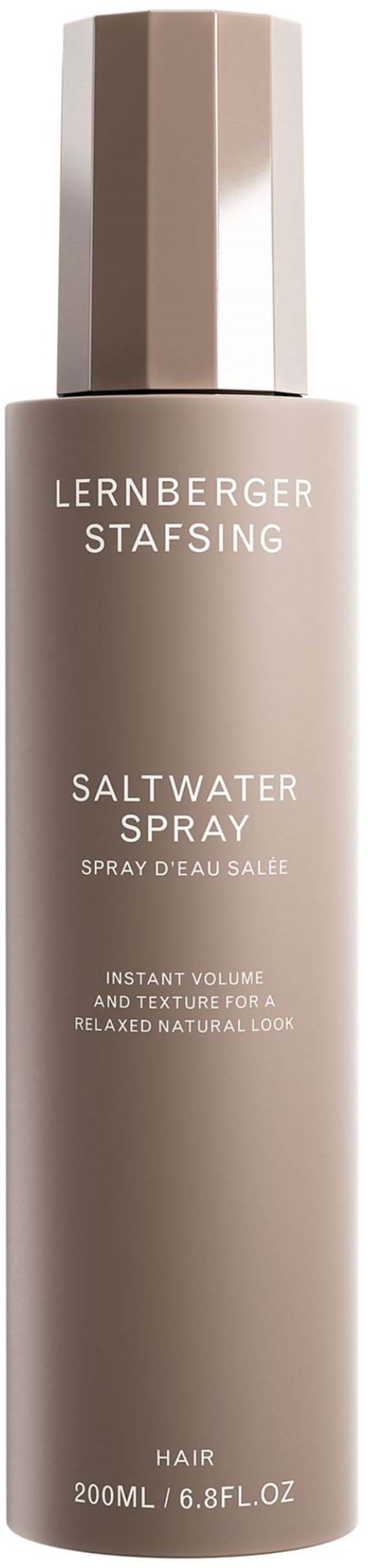 Pitkä, beigen värinen suihkepullo, jossa lukee "Saltwater Spray" hiuksille, käytetään luonnollisen ja rentoon ilmeeseen.