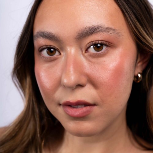 Eine junge Frau mit heller Haut, braune Haare und braune Augen schaut direkt in die Kamera. Sie trägt natürlichen Make-up und kleine Ohrringe.