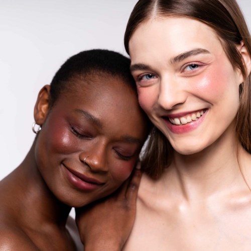 Zwei Frauen stehen nah beieinander, lächeln sanft und zeigen Freundschaft und Komfort.