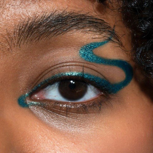 A close-up of a person's eye with teal and blue eye makeup, and a decorative swirl design on the eyelid.