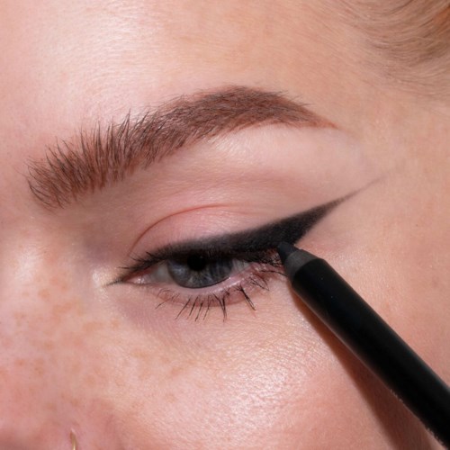 Eine Person zieht schwarzen Eyeliner auf das obere Augenlid mit einem stiftähnlichen Werkzeug.