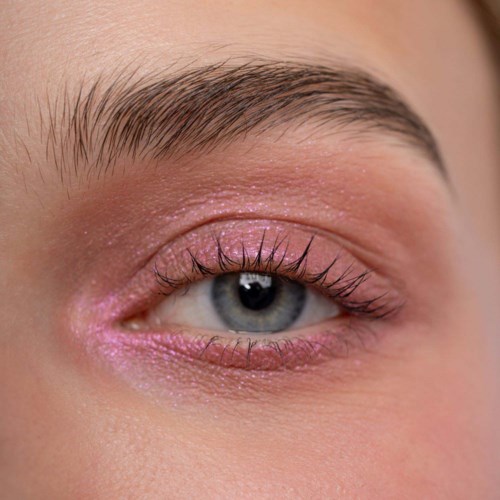 Close-up of a blue eye with long lashes and pink makeup on eyelid and lower lash line.