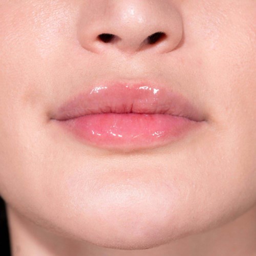 Nahaufnahme von Lippen mit glänzender, hellrosa Lipgloss und glatter Haut.