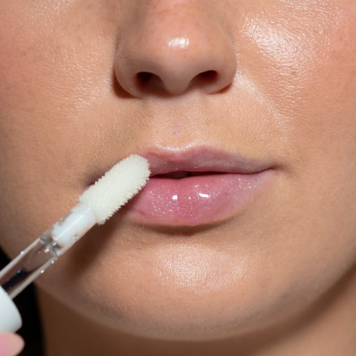 Eine Person trägt Lipgloss mit einem Pinsel auf glänzende Lippen auf.