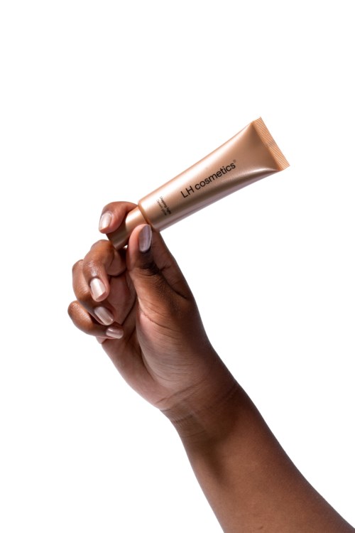 Käsi pitää beigeä putkilua, jossa lukee 'LH cosmetics', taustalla valkoinen.