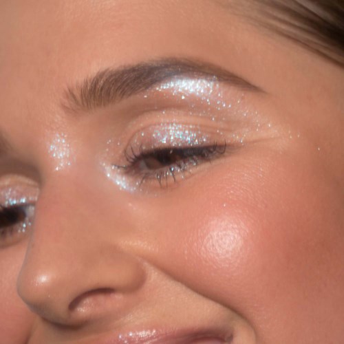 Eine Frau trägt funkelndes Augen-Make-up mit leuchtender Wange und gepflegten Augenbrauen.