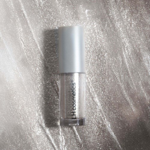 Ein transparenter Lipgloss mit weißem Deckel auf einer glitzernden silbernen Oberfläche.