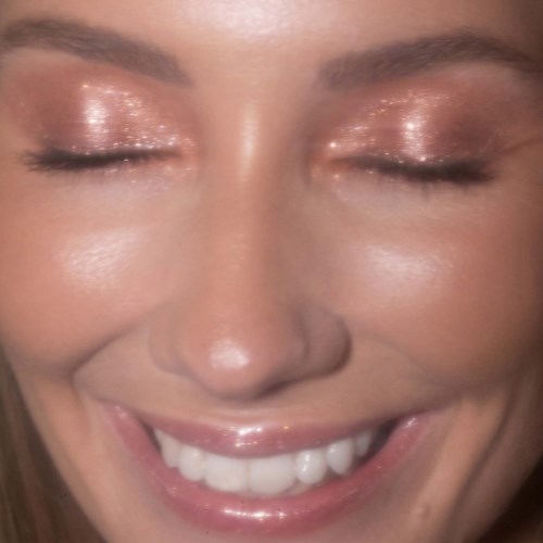 Eine Frau mit Glitzer-Lidschatten, lächelnd mit geschlossenen Augen und Zähnen.