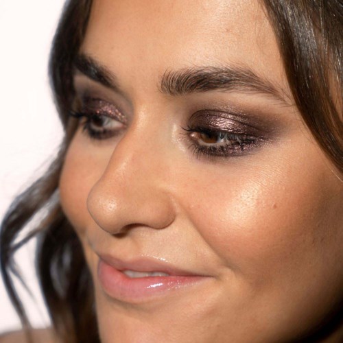  Nahaufnahme einer Frau mit glänzendem Make-up, lächelt sanft, zeigt ihr Gesicht im weichen Licht.
