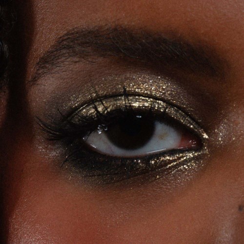 Nahaufnahme eines Auges mit glitterfarbenem Gold- und Schwarz-Augen-Make-up, langen Wimpern und gepflegten Augenbrauen.