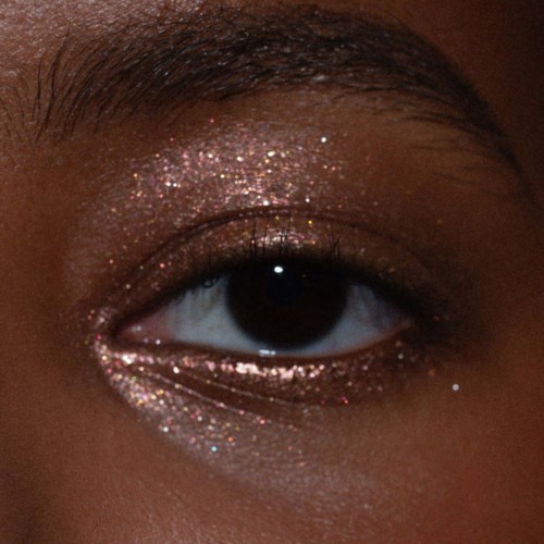 Nahaufnahme eines Auges mit glitzernder Lidschatten und gepflegten Augenbrauen.