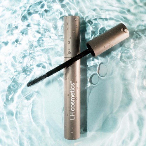 Ein Mascara-Röhrchen schwimmt im Wasser mit Bürste nach außen, Wassertröpfchen auf der Verpackung.