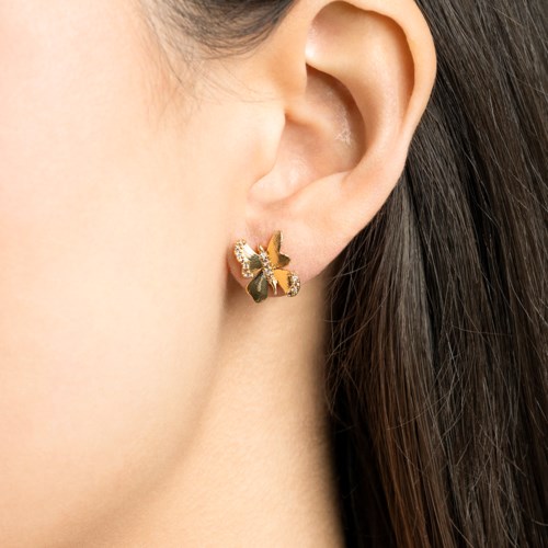 A close-up of a woman's ear with a gold butterfly-shaped earring. The earring has small shiny stones. The woman has brown hair.
