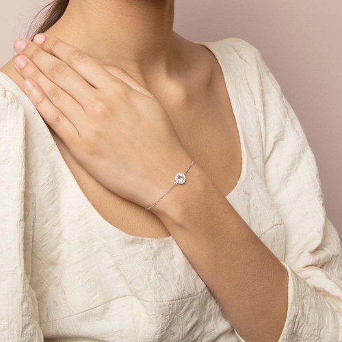 A person wears a white top and a delicate bracelet with a small round charm on their wrist.