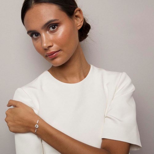 A woman with brown hair in a bun, wearing a white top, looks at the camera with a subtle smile.