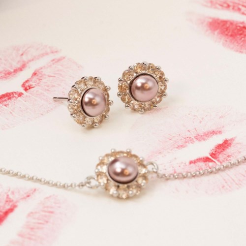 Elegant jewelry set with pink pearls and surrounding clear stones, includes earrings and a necklace, on a white and pink background.