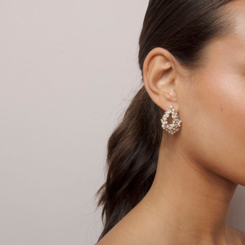 A woman with dark hair wears a large, sparkling earring shaped like a teardrop.