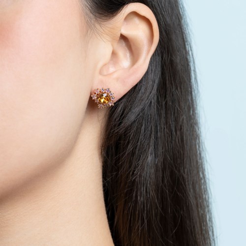 A woman wears a gold flower-shaped earring with a large yellow gemstone in the center.