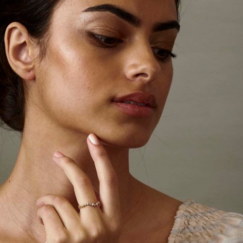 A woman gently touches her chin, with clear skin and relaxed expression, looking to the side.