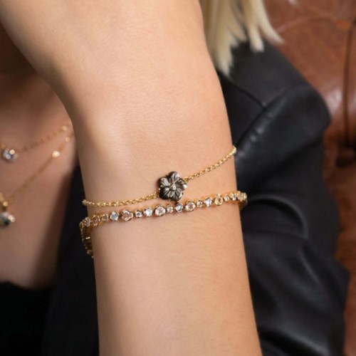 Two gold bracelets, one with a flower charm and the other with clear gemstones, worn on a person's wrist.