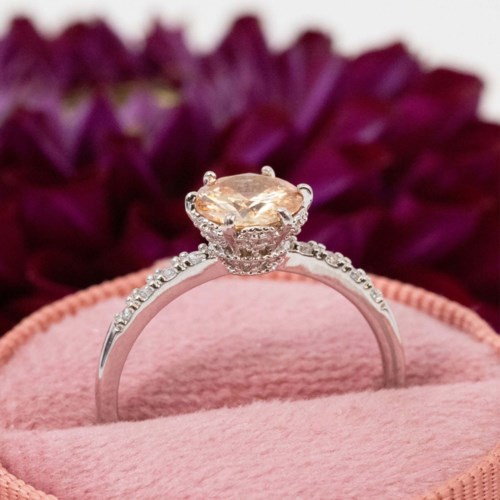 Elegant engagement ring with a large central gemstone and smaller surrounding stones on a pink velvet cushion.